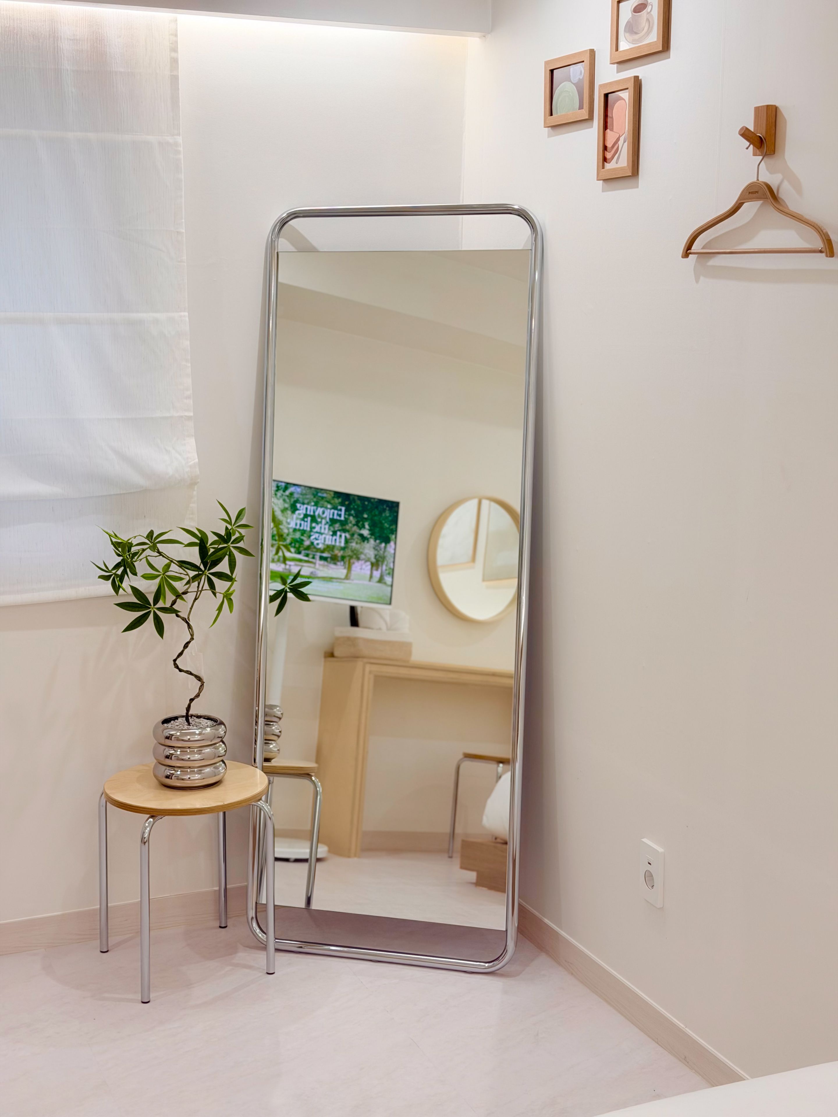 A bathroom with a large mirror, a small stool, a potted plant, and a framed picture on the wall.