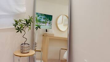 A bathroom with a large mirror, a small stool, a potted plant, and a framed picture on the wall.