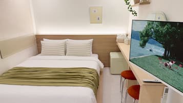 A hotel room with a bed, a desk with a computer, a TV, and a small table with chairs.