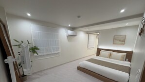 A hotel room with a bed, a window with a white curtain, an air conditioning unit, and a small potted plant. - Stay Zam Hotel (Jung-gu)