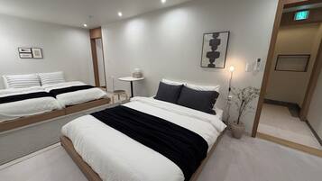 A modern hotel room with two beds, a small table, a wall-mounted light, and a potted plant.