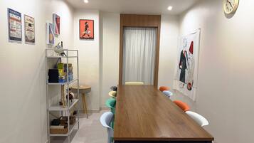 A dining area with a wooden table, colorful chairs, a shelf with boxes, and a clock on the wall.