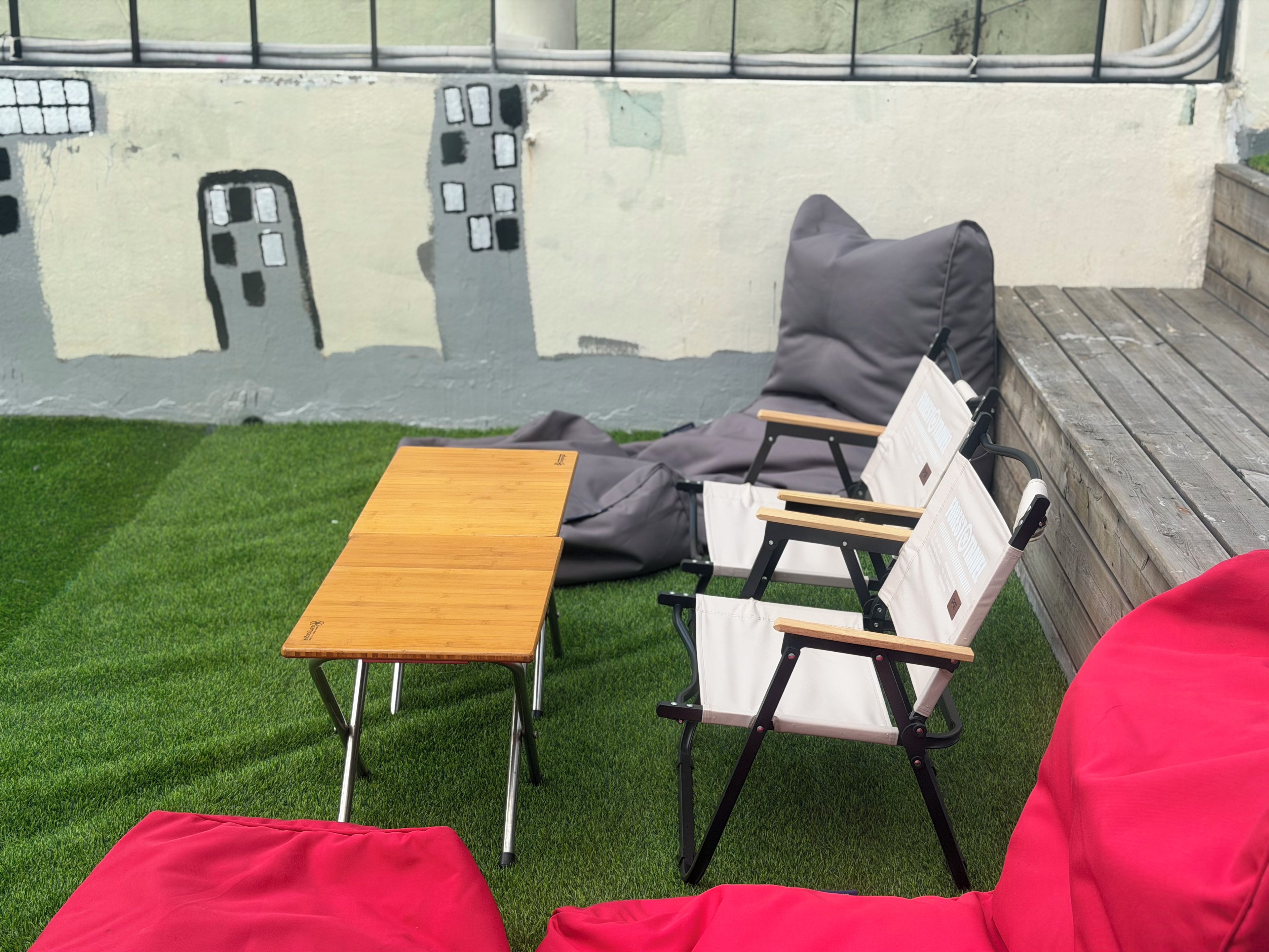 Un espace détente avec une table en bois et deux chaises, un coussin rouge et une fresque murale.