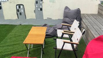 Un espace détente avec une table en bois et deux chaises, un coussin rouge et une fresque murale.