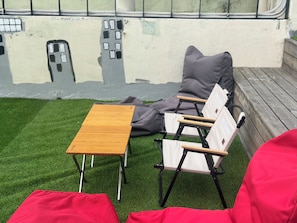 Un área de estar con una mesa de madera y dos sillas, un cojín rojo y un mural en la pared.