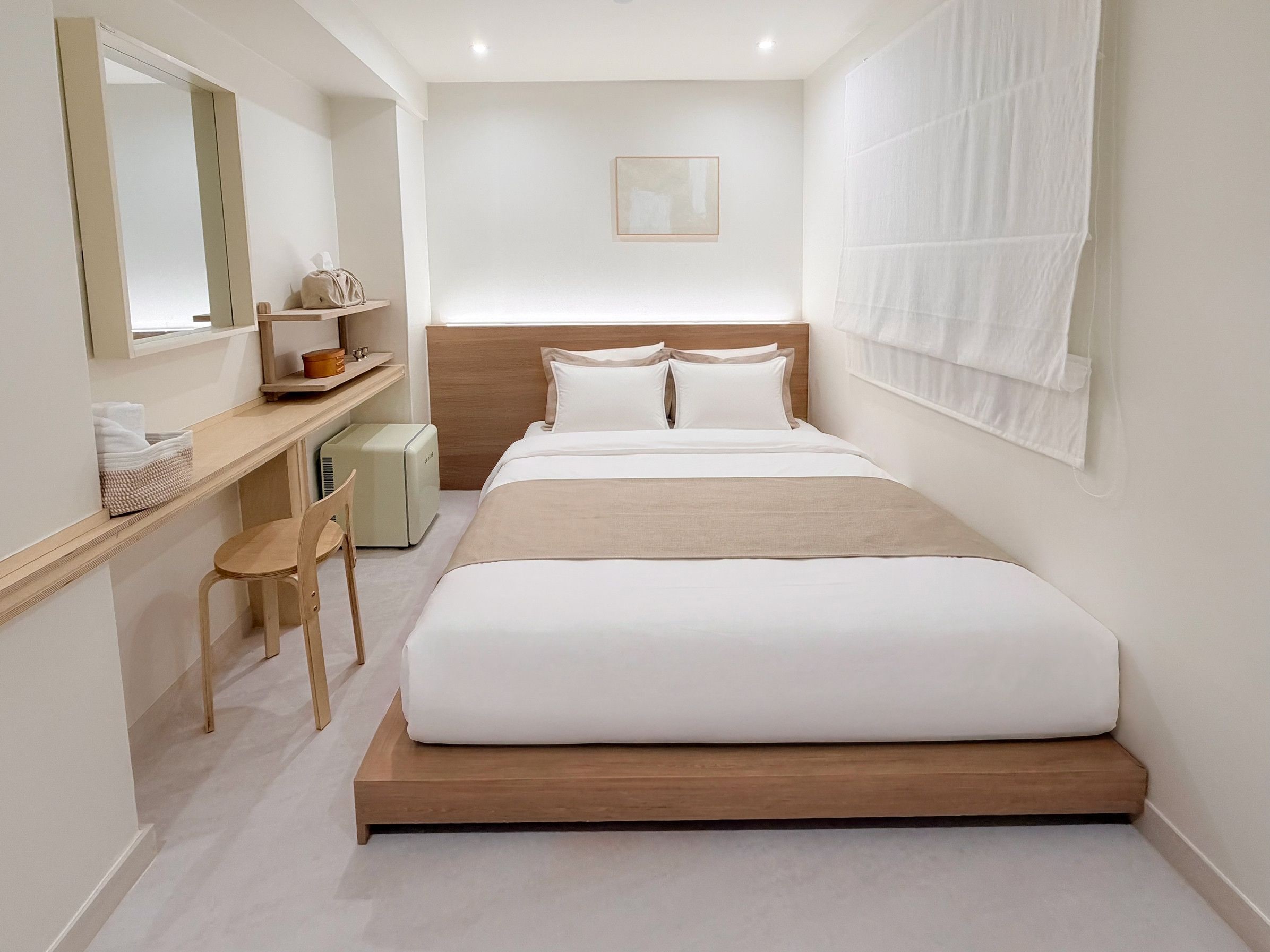 A modern hotel room with a bed, a desk, a chair, and a small heater.
