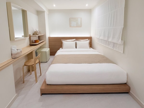 Una habitación de hotel moderna con cama, escritorio, silla y un pequeño calentador.