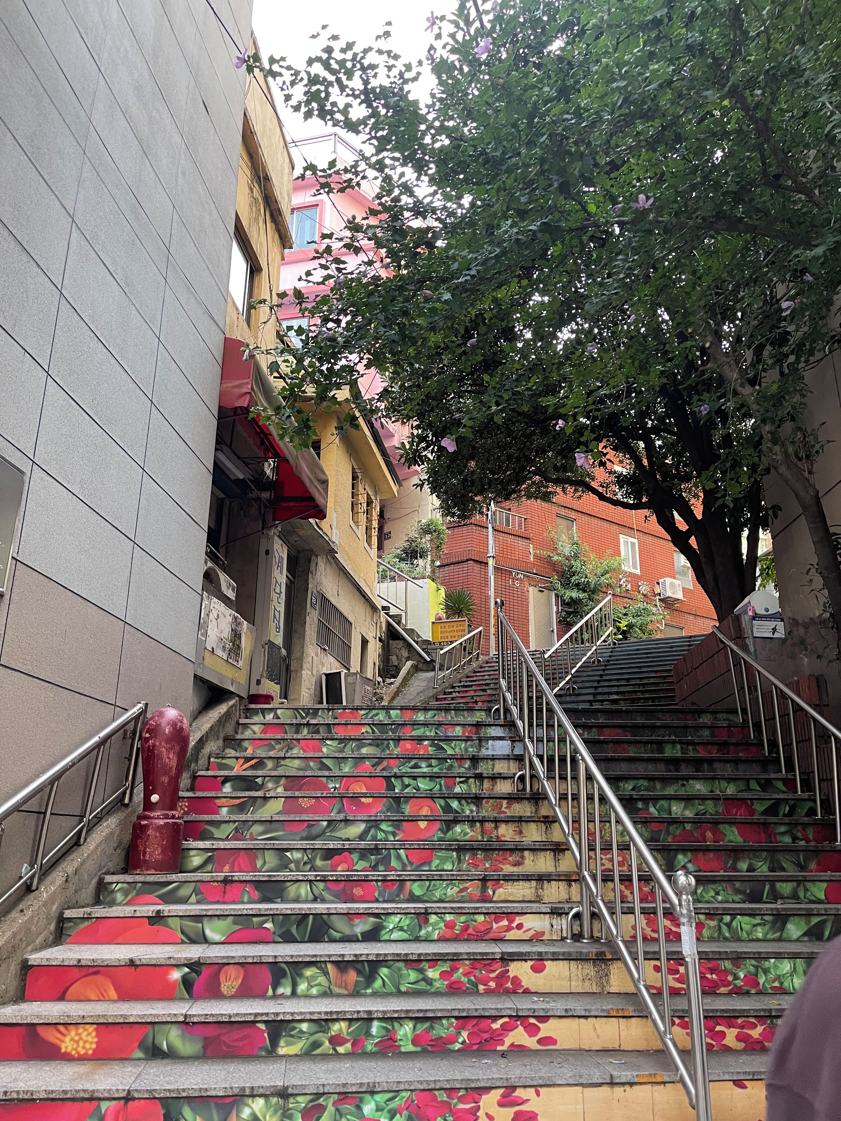 Escadaria com design floral, corrimão de metal e edifícios ao fundo.