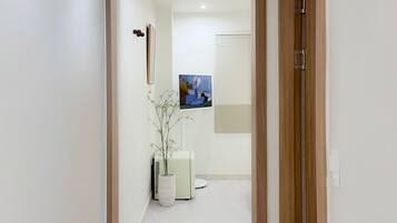A hallway with a wooden door frame, a white wall, a framed picture, a potted plant, and a small rug.