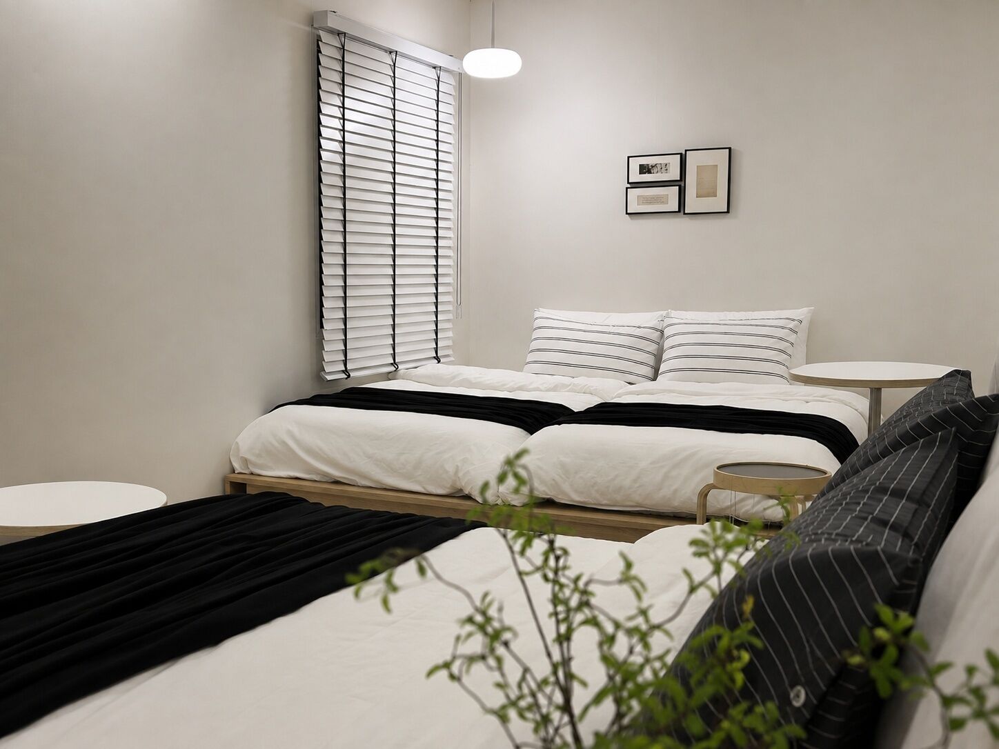 A modern bedroom with a bed, bedside tables, a round table, and a window with blinds.