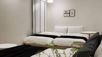 A modern bedroom with a bed, bedside tables, a round table, and a window with blinds.