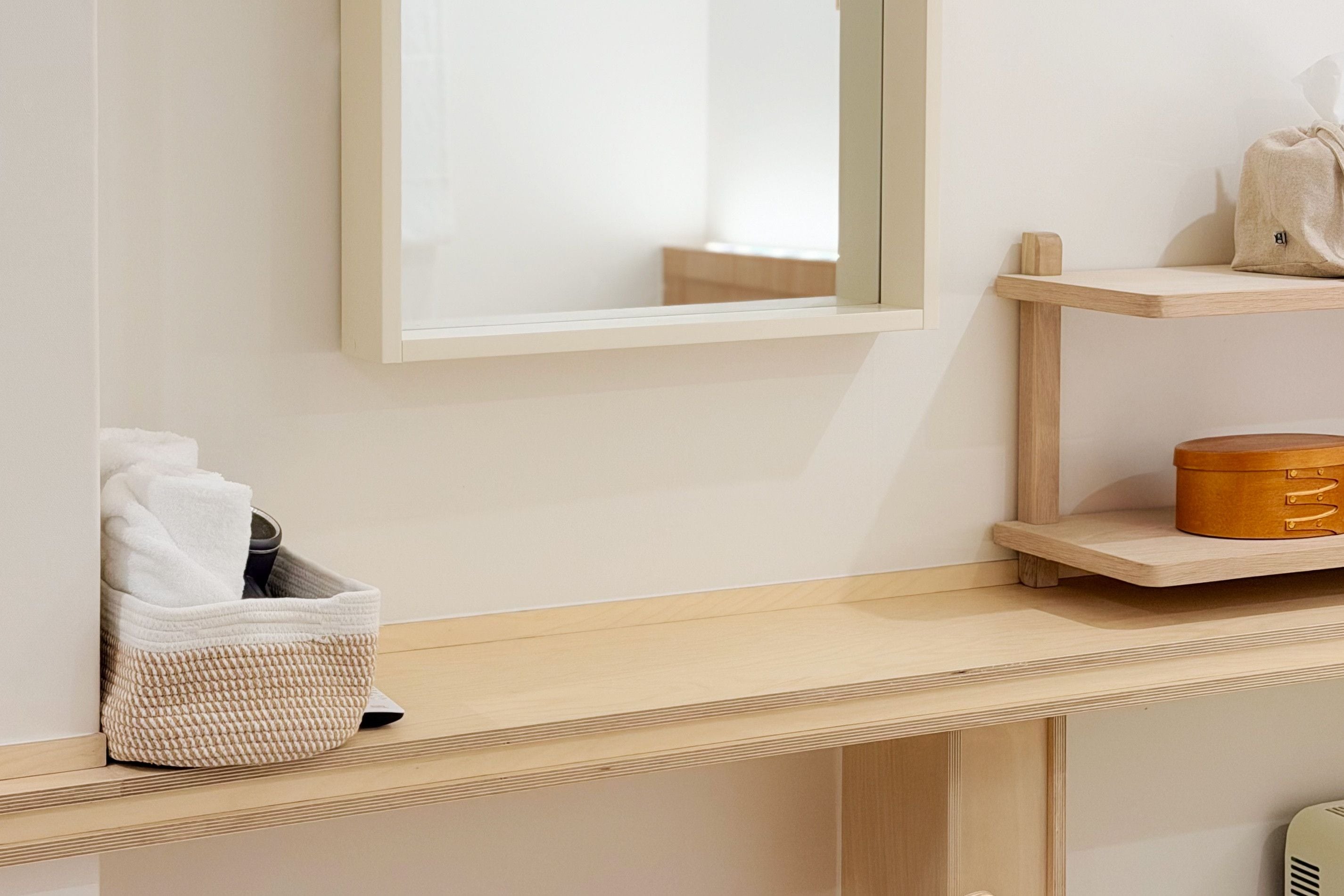 A bathroom with a wooden vanity, a mirror, a towel rack, and a shelf with a container.