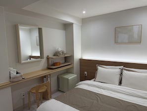 Een hotelkamer met een bed, een bureau, een stoel, een kleine verwarming en een spiegel.