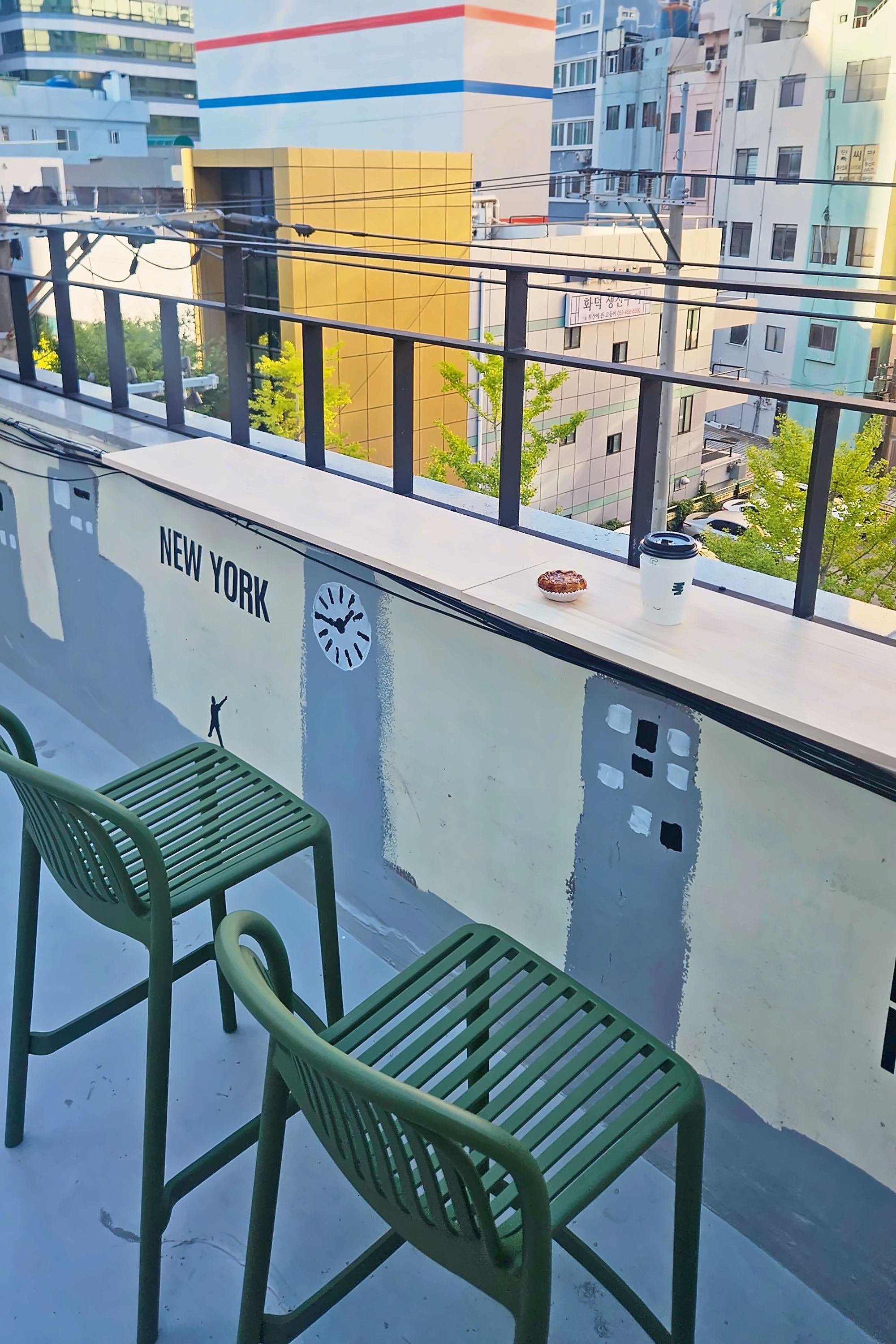 A balcony with two green chairs, a clock, and a sign reading 'NEW YORK'.
