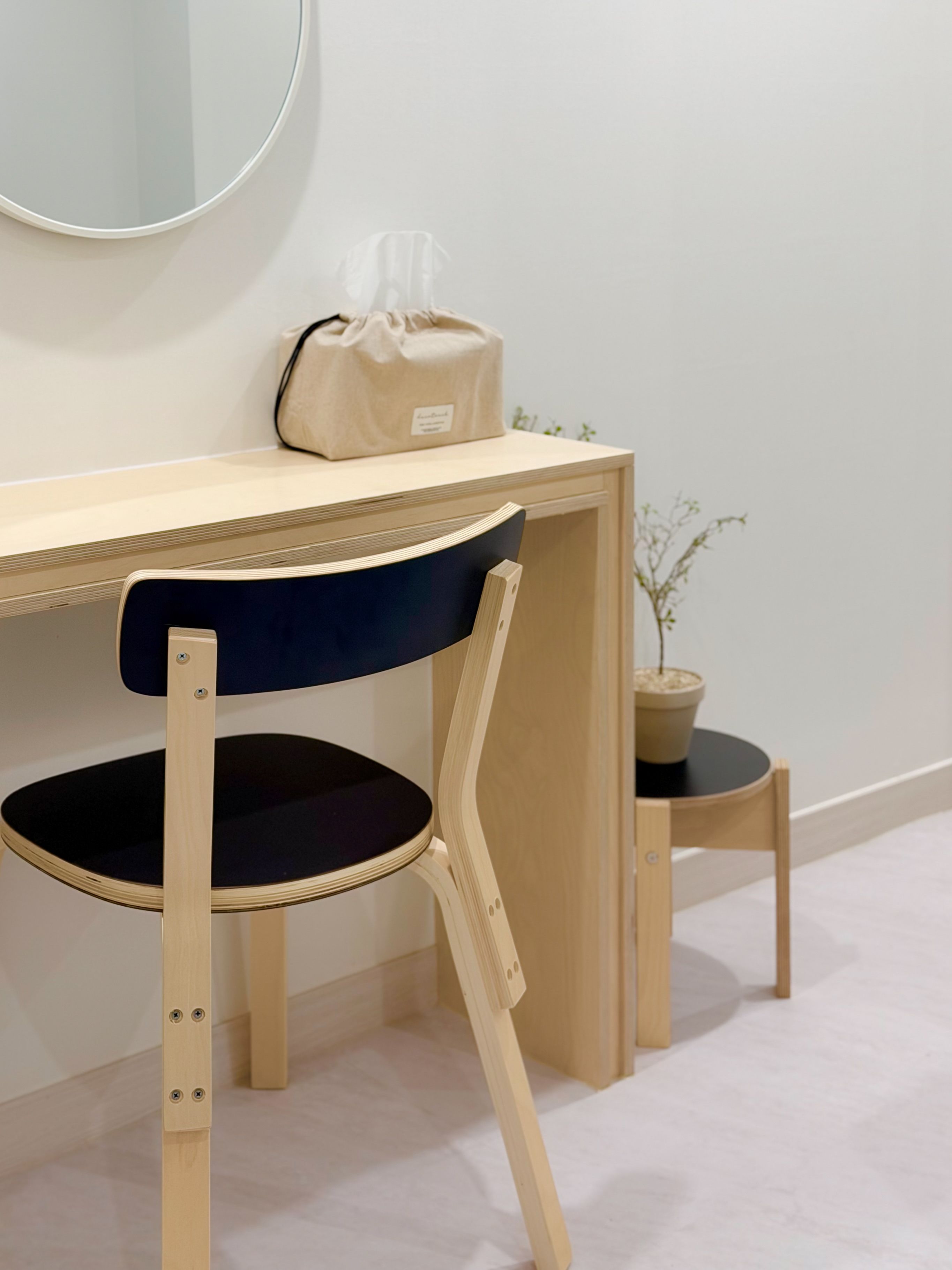 A wooden desk with a chair, a small stool, a potted plant, and a bag on the desk.