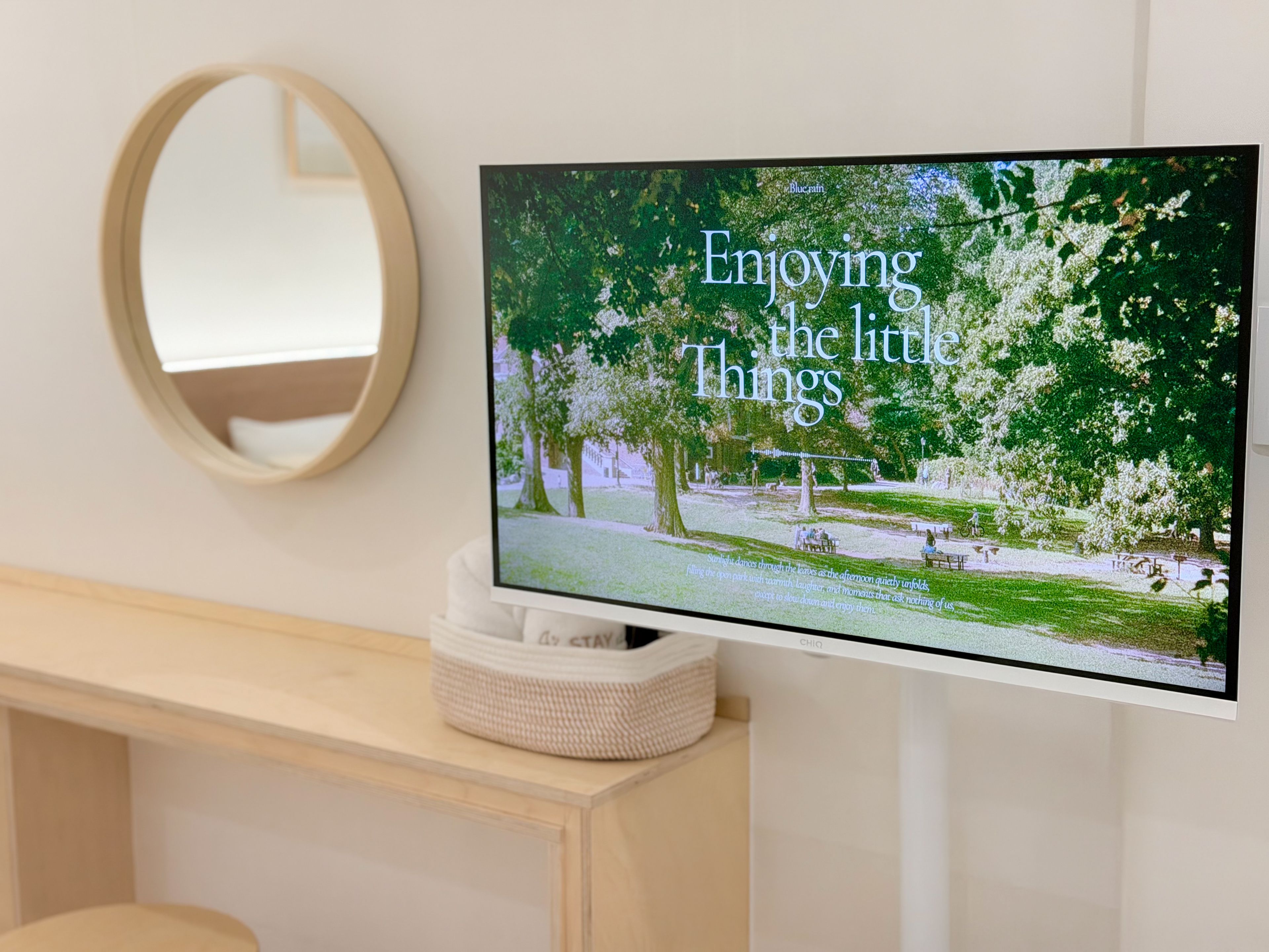 A television mounted on a wall displaying a nature scene with the text 'Enjoying the little things.'