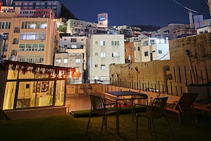 Une terrasse sur le toit, avec une table et des chaises, d’où l’on peut admirer la vue sur la ville illuminée la nuit.