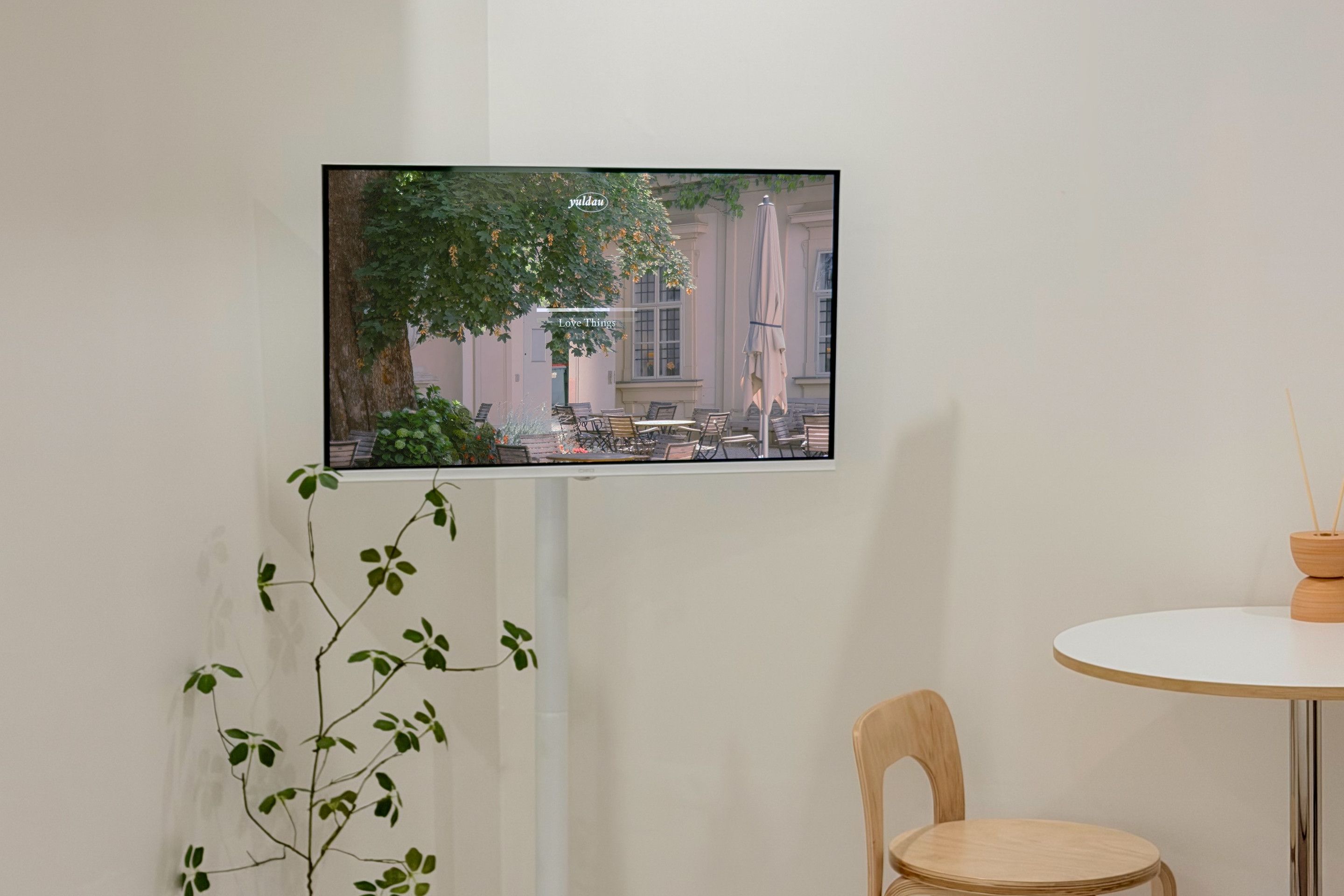 Un televisor montado en la pared muestra una escena al aire libre con un árbol y un edificio.