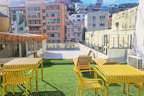 Une terrasse sur le toit avec des chaises et des tables jaunes, un petit espace aménagé en jardin et une vue sur les bâtiments environnants.