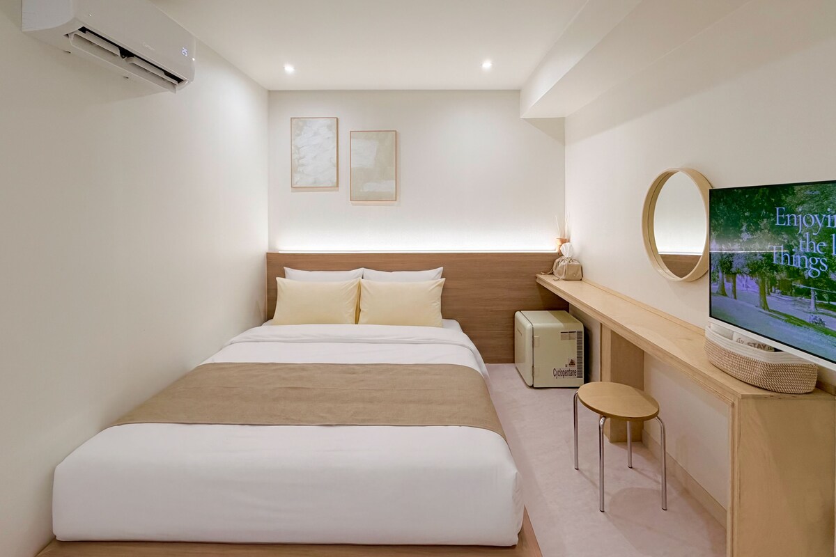 A hotel room with a bed, a television, a small table, and a wall-mounted mirror.