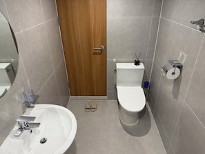 Een badkamer met een houten deur, toilet, bidet, wastafel met kraan en een paar slippers op de vloer.