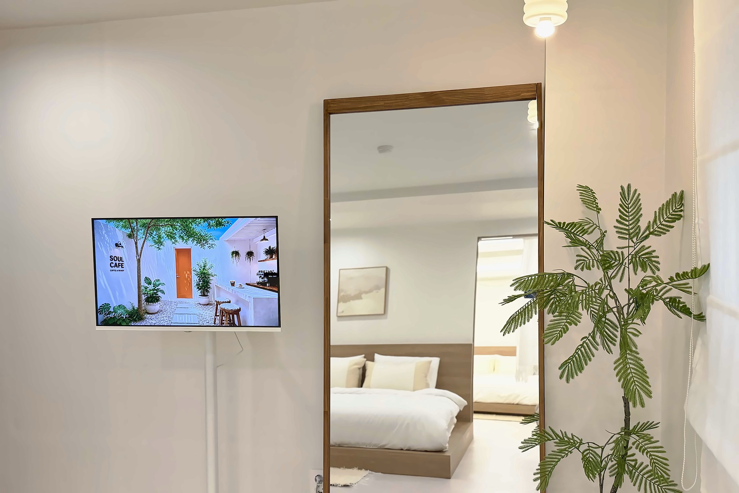 Een hotelkamer met een bed, een grote spiegel, een televisie waarop een café te zien is, en een potplant.