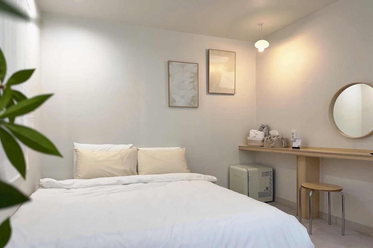 Una habitación de hotel con una cama, una mesita de noche, un espejo y un taburete pequeño.