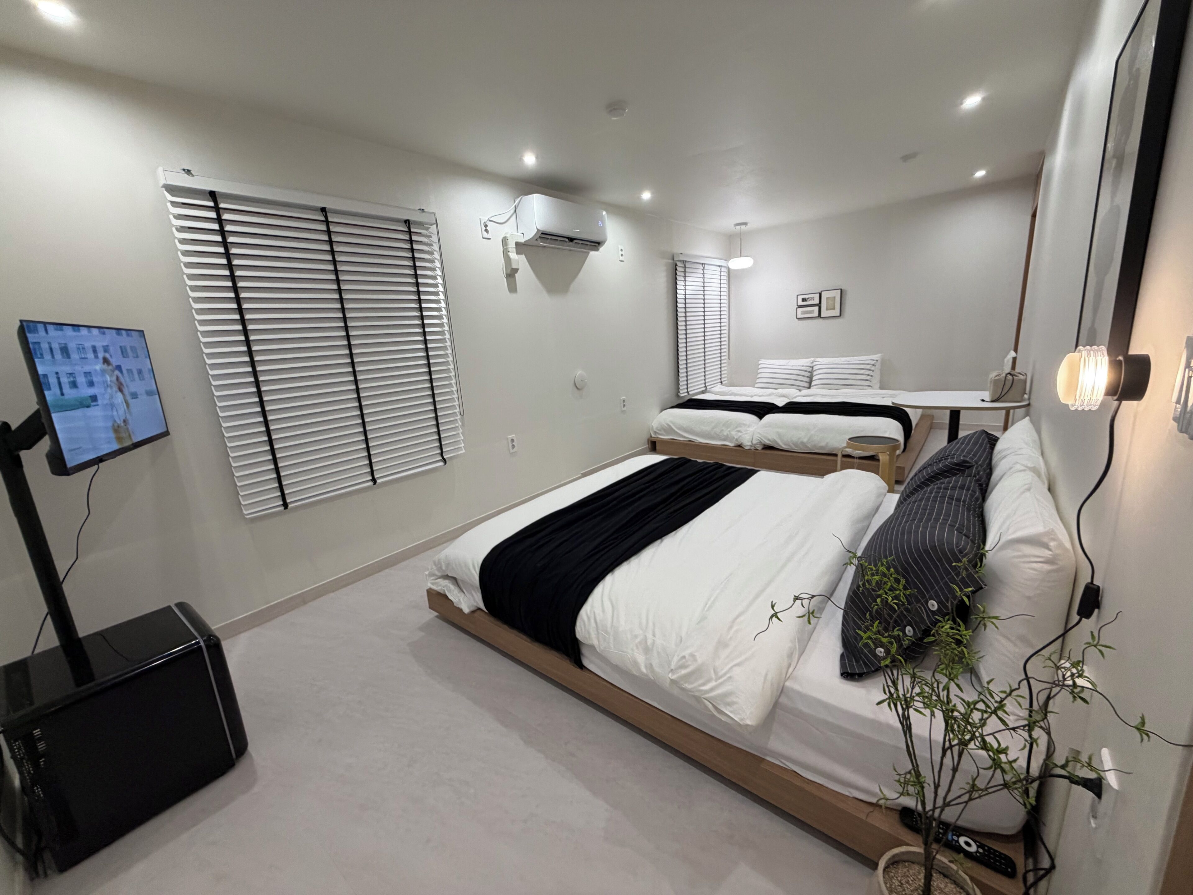 A modern bedroom with a bed, bedside table, wall-mounted air conditioning unit, and a television on a stand.