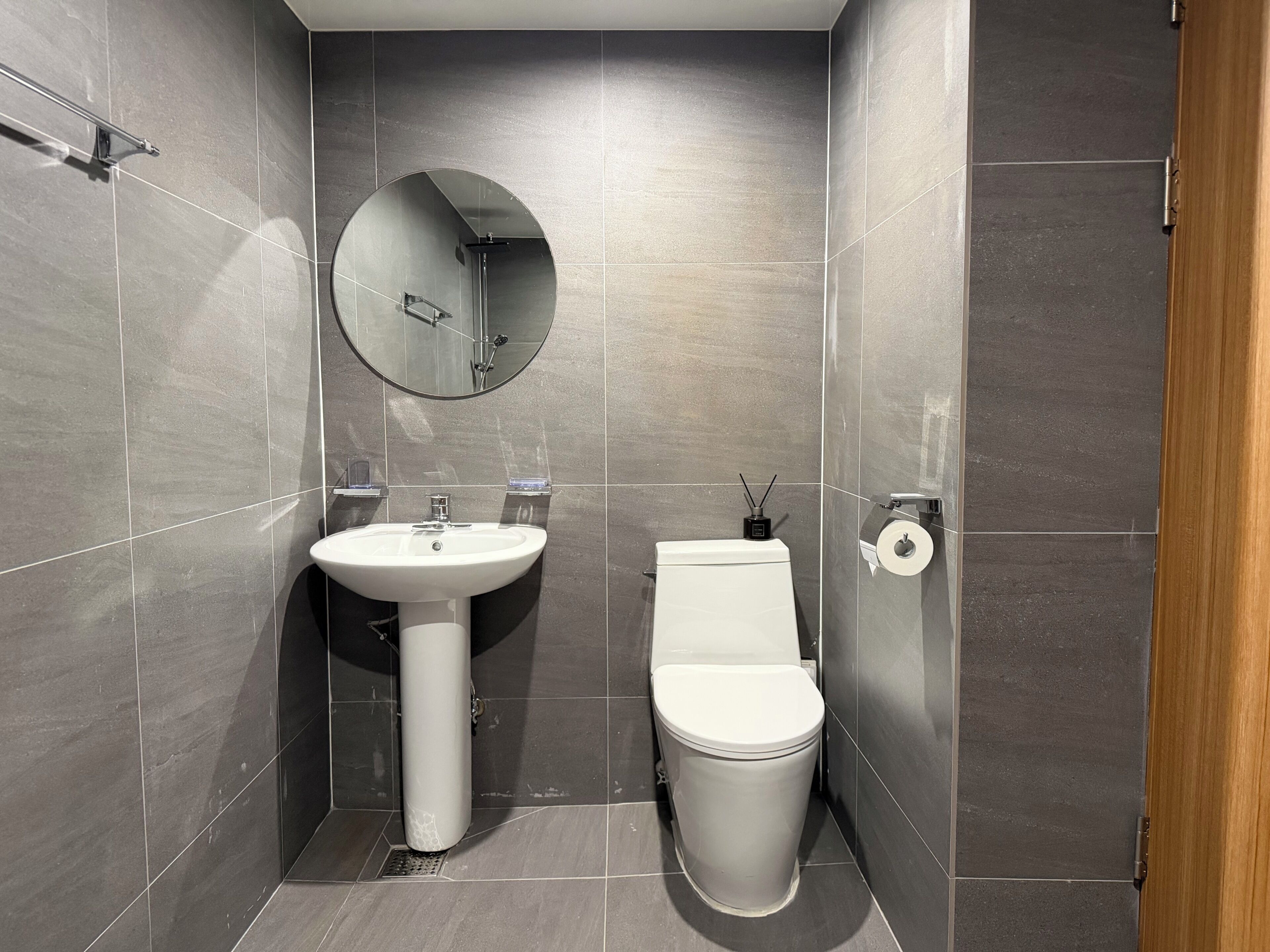 A modern bathroom with a white sink, toilet, and a round mirror on the wall.