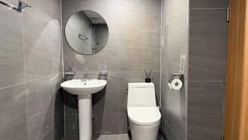 A modern bathroom with a white sink, toilet, and a round mirror on the wall.