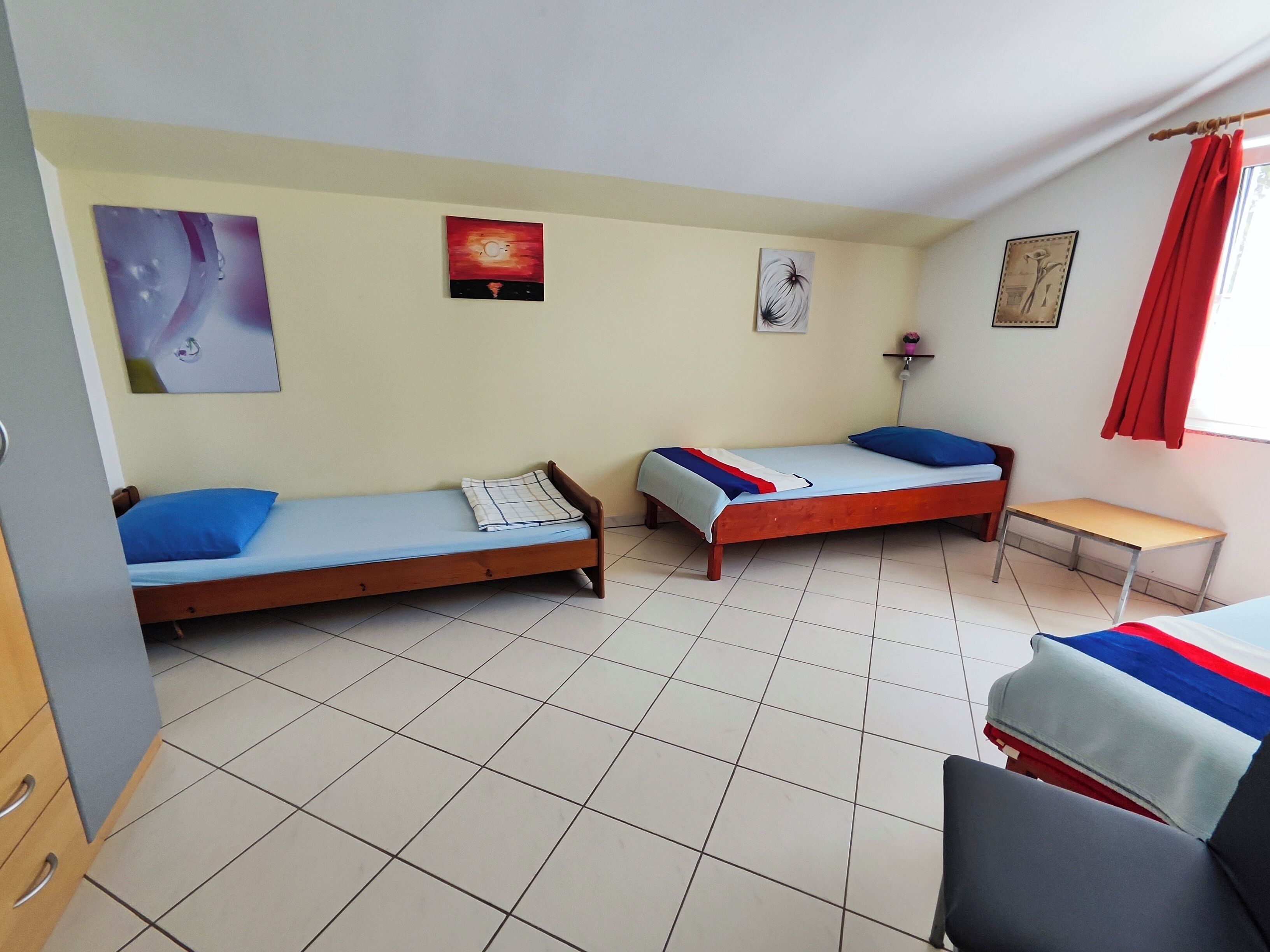 A dormitory room with two single beds, a desk, and a chair.