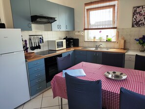 A compact kitchen with a refrigerator, microwave, and Bosch dishwasher. There is a dining table with a red and white checkered tablecloth and blue chairs. - Ferienwohnung "Dorade" villa Riba in Pula ruhig trotzdem Zentrum und Meeresnähe (Pula)