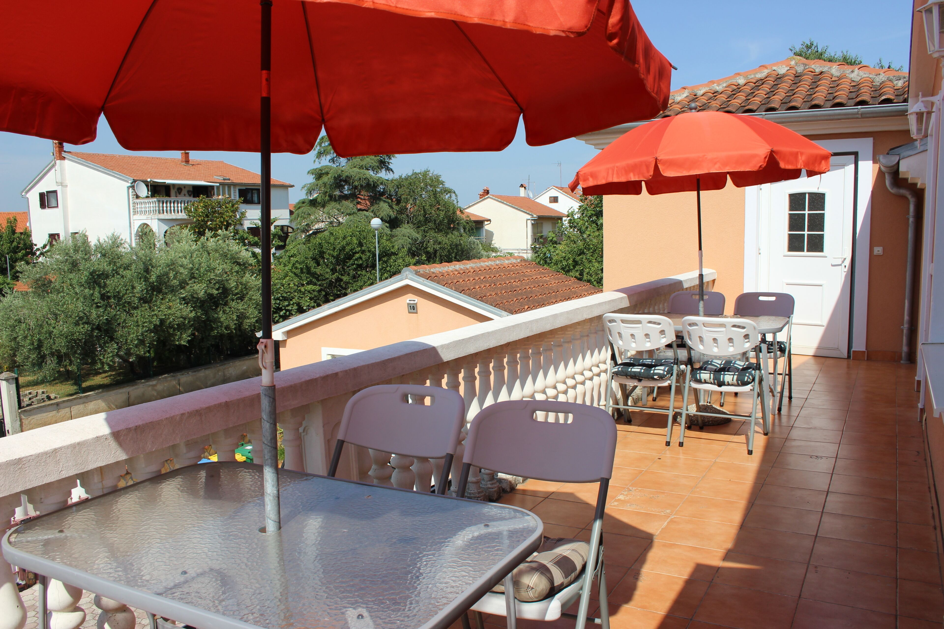 Una terraza con mesa y sillas, sombrillas rojas y vistas de edificios circundantes.