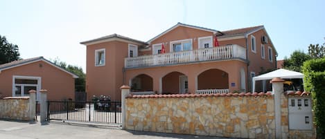A two-story building with a stone facade, a balcony with railings, and a gated entrance.