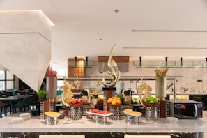 Een moderne hotellobby met een marmeren receptiebalie, decoratieve vazen en een groot abstracte sculptuur.
