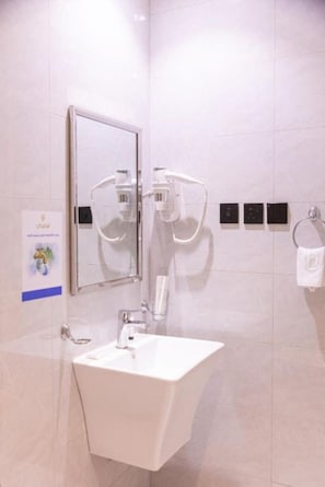 Een moderne badkamer met een wit wastafelmeubel, een spiegel en een aan de muur bevestigde haardroger.