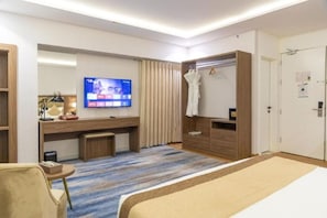 Een hotelkamer met een bed, een bureau, een televisie, een badjas en een kledingkast.