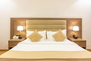 Een hotelkamer met een groot bed, twee nachtkastjes met lampen en een houten hoofdeinde.