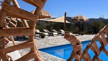 A pool area with a wooden lattice structure, lounge chairs, and a clear blue sky.