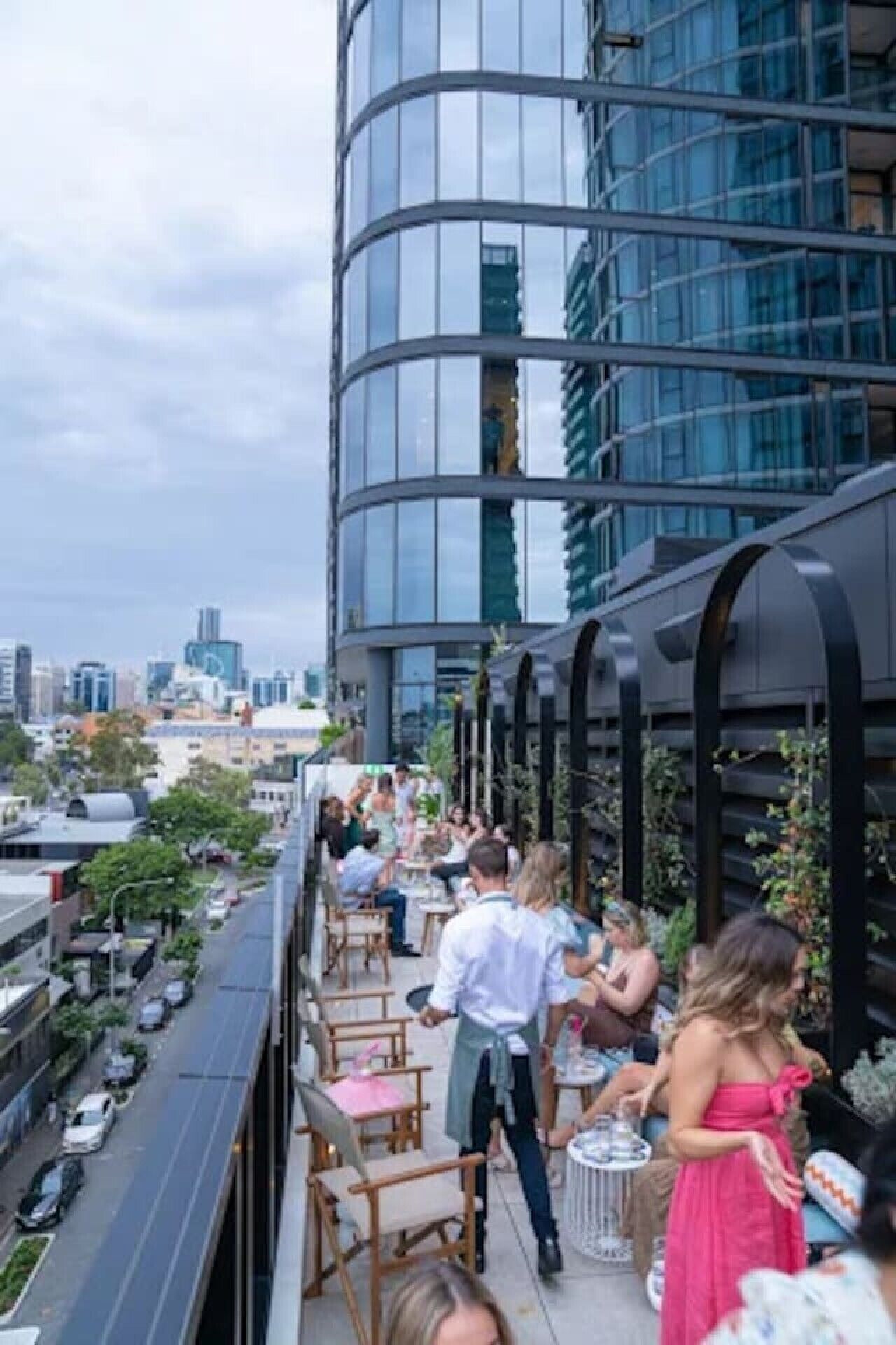 A rooftop bar with outdoor seating, a cityscape view, and a modern building structure.