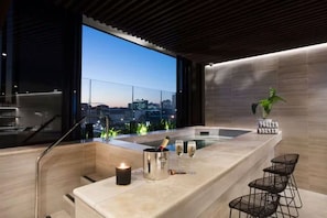 A modern bathroom with a large window, a bathtub, a sink, and a bar area with a candle and champagne glasses. - The Skyline Residence on the 23rd Floor (Fortitude Valley)