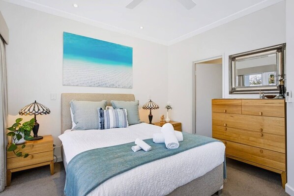 A bedroom with a bed, bedside tables, a dresser, a mirror, and a painting on the wall.