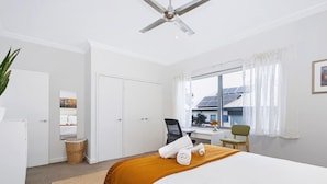 A hotel room with a bed, a desk, a chair, a wardrobe, a ceiling fan, and a window with curtains. - Leederville Life - 2 Bedroom House (West Leederville)