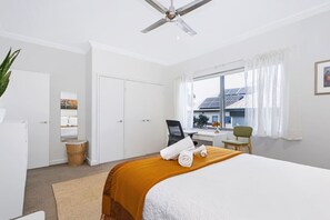 A hotel room with a bed, a desk, a chair, a wardrobe, a ceiling fan, and a window with curtains. - Leederville Life - 2 Bedroom House (West Leederville)