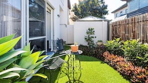A residential backyard with a small lawn, a patio table with chairs, and various potted plants. - Leederville Life - 2 Bedroom House (West Leederville)