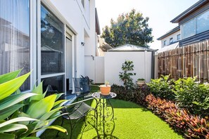 A residential backyard with a small lawn, a patio table with chairs, and various potted plants. - Leederville Life - 2 Bedroom House (West Leederville)