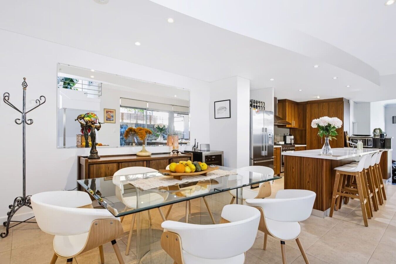 A modern kitchen with a glass dining table, white chairs, and wooden cabinets.