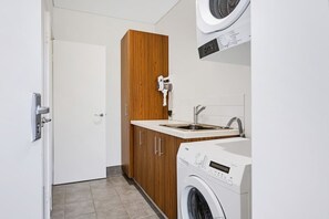 A compact laundry room with a washing machine, a sink, and wooden cabinetry.