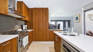 A modern kitchen with wooden cabinets, a stove, microwave, and a sink. - Leederville Life - 2 Bedroom House (West Leederville)