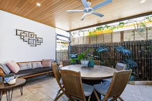An outdoor patio with a round table, chairs, a ceiling fan, and a bamboo fence.